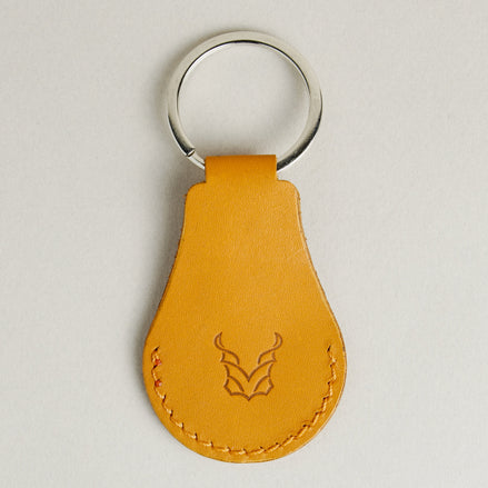 Back view of amber AirTag keychain in full-grain leather with round metal key ring and embossed logo. Markore Tag Mate.