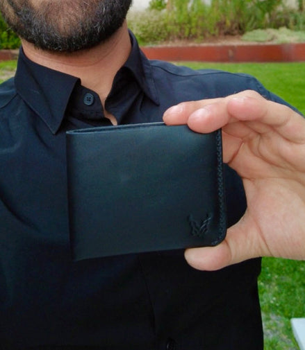 Man holding a black markore assam silk wallet made with premium full grain leather outdoors with greenery in the background