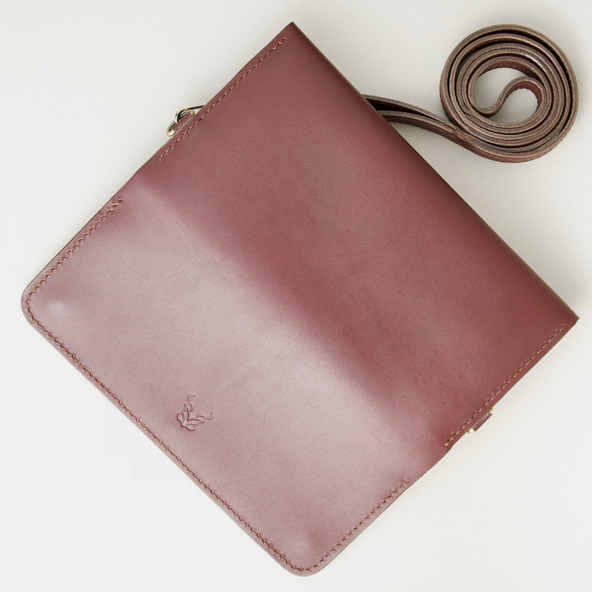 Unfolded outside view of horizontal full-grain leather crossbody bag and matching shoulder strap in Espresso Brown, showing handmade stitching and embossed logo. Markore Gul Sahar.