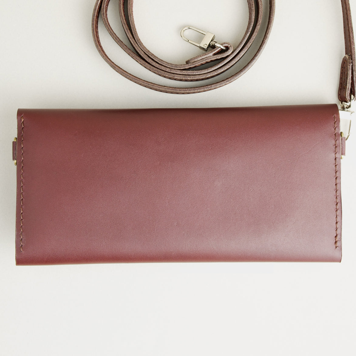 Backside view of horizontal full-grain leather crossbody bag and matching shoulder strap in Espresso Brown, showing handmade stitching. Markore Gul Sahar.