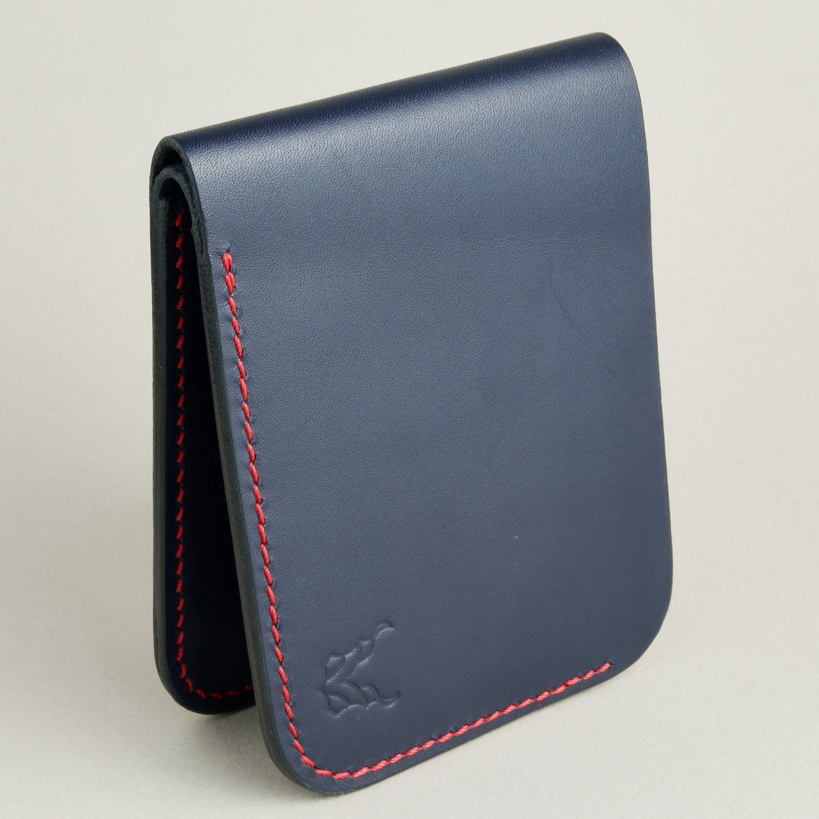Side view of full-grain leather bifold wallet with hand-stitched red thread in Dark Blue and embossed logo. Markore Hunza Arc.