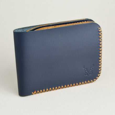 Side view of dark blue full-grain leather bifold wallet featuring handmade amber cross-stitched detailing on the edges and embossed logo. Markore Hunza Edge.