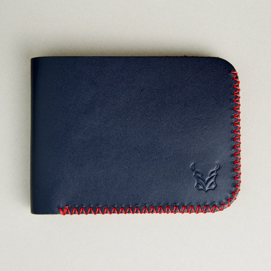 Front view of dark blue full-grain leather bifold wallet featuring handmade red cross-stitched detailing on the edges and embossed logo. Markore Hunza Edge.