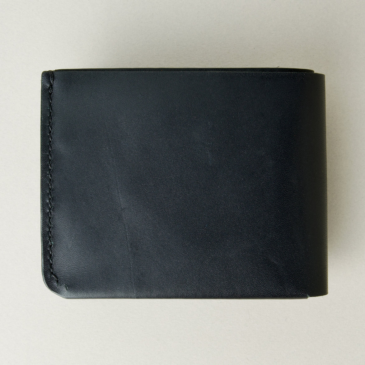 Back view of midnight black full-grain leather wallet featuring a seamless bottom edge and handmade stitching. Markore Assam Silk.