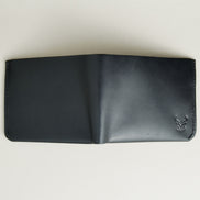 Outside view of midnight black full-grain leather wallet featuring a seamless bottom edge, handmade stitching and embossed logo. Markore Assam Silk.