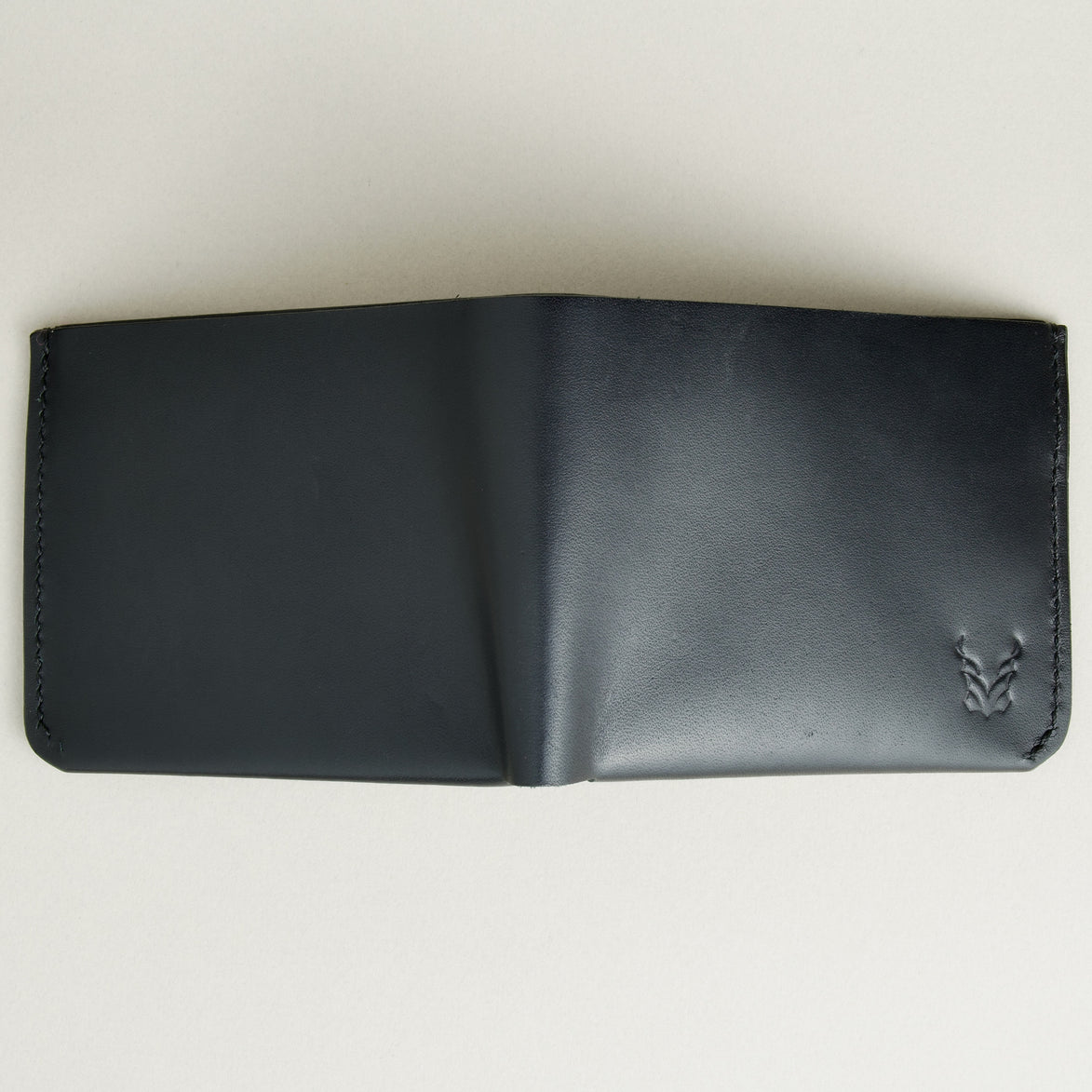 Outside view of midnight black full-grain leather wallet featuring a seamless bottom edge, handmade stitching and embossed logo. Markore Assam Silk.
