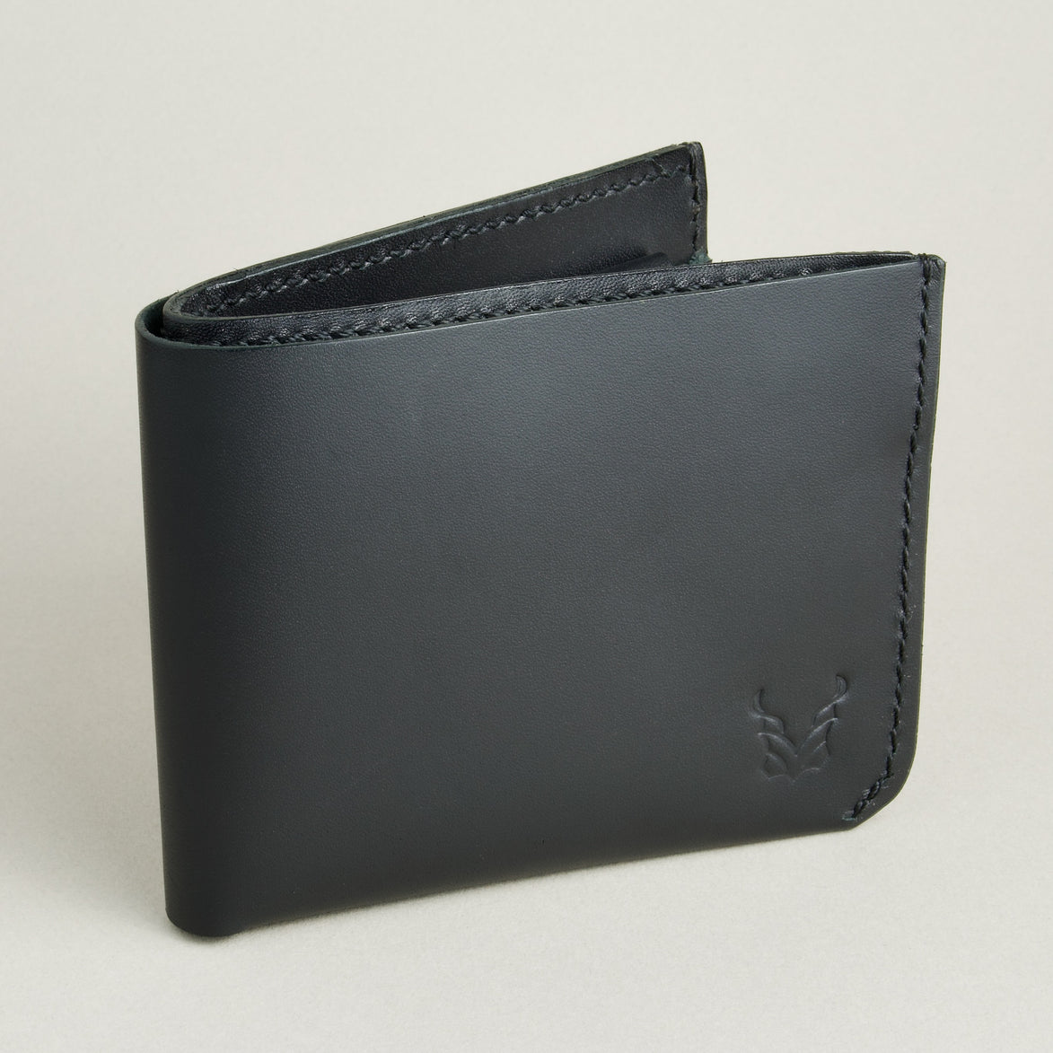 Side view of midnight black full-grain leather wallet featuring a seamless bottom edge, handmade stitching and embossed logo. Markore Assam Silk.
