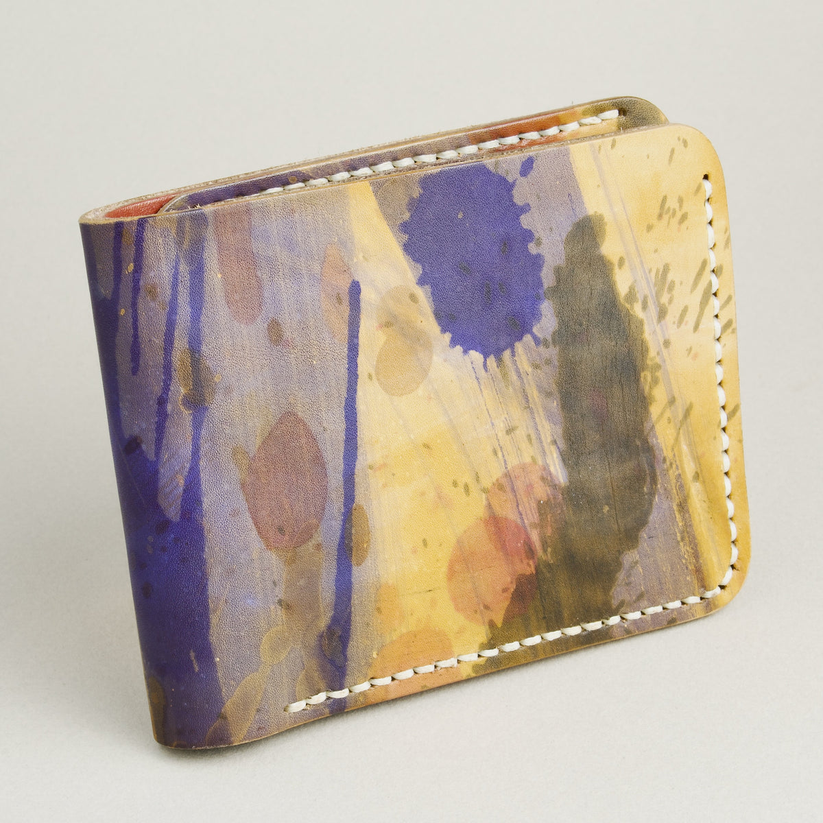 Side view of hand-painted full-grain leather bifold wallet in purple, amber, and brown, featuring handmade stitching. Markore Canvas Chaos.