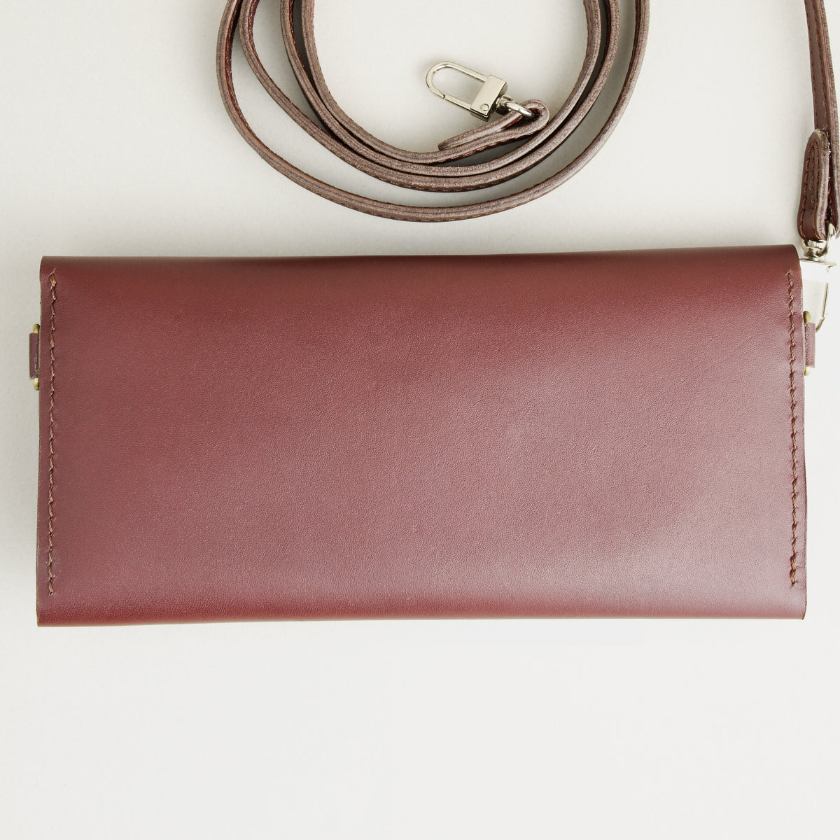Backside view of horizontal full-grain leather crossbody bag and matching shoulder strap in Espresso Brown, showing handmade stitching. Markore Gul Sahar.