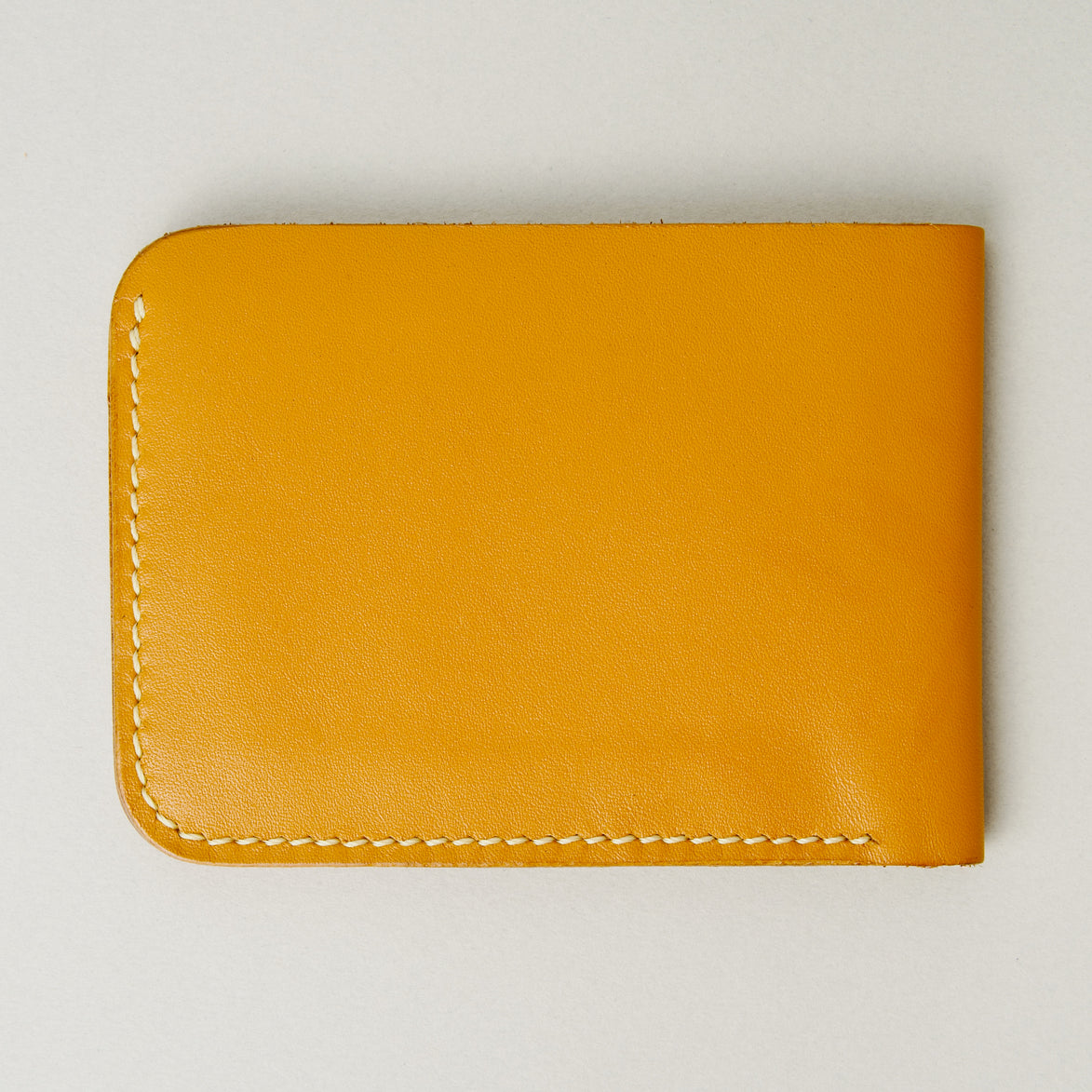 Back view of full grain leather bifold wallet in amber, featuring ivory handmade stitching. Markore Hunza Fold.