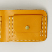 Detail of full grain leather bifold wallet in amber, featuring ivory handmade stitching and a coin pocket with a brass press stud. Markore Hunza Fold.