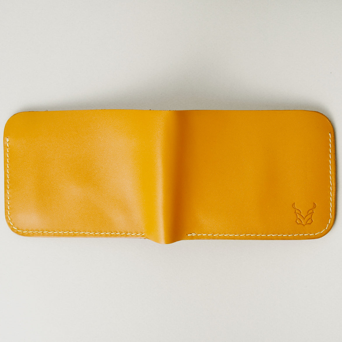 Outside view of full grain leather bifold wallet in amber, featuring ivory handmade stitching and embossed logo. Markore Hunza Fold.