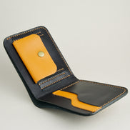 Inside view of full grain leather bifold wallet in midnight black, featuring handmade stitching, a coin pocket with brass press stud and card slots in amber. Markore Hunza Fold.