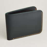 Side view of full grain leather bifold wallet in midnight black, featuring amber handmade stitching and embossed logo. Markore Hunza Fold.