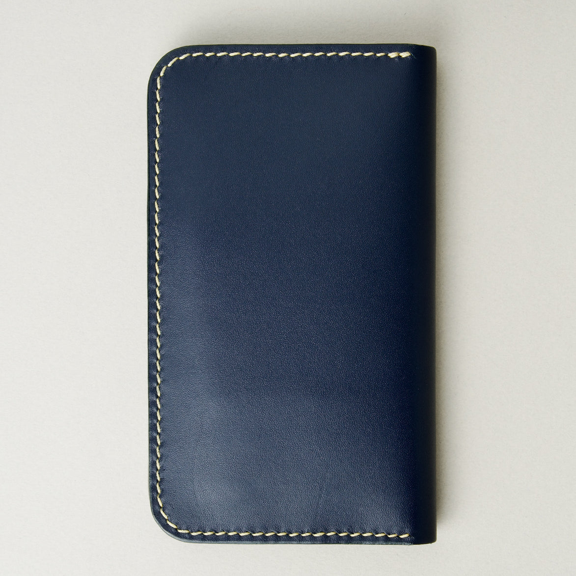 Back view of vertical full-grain leather bifold wallet in dark blue, featuring handmade stitching in ivory. Markore Karakoram II.