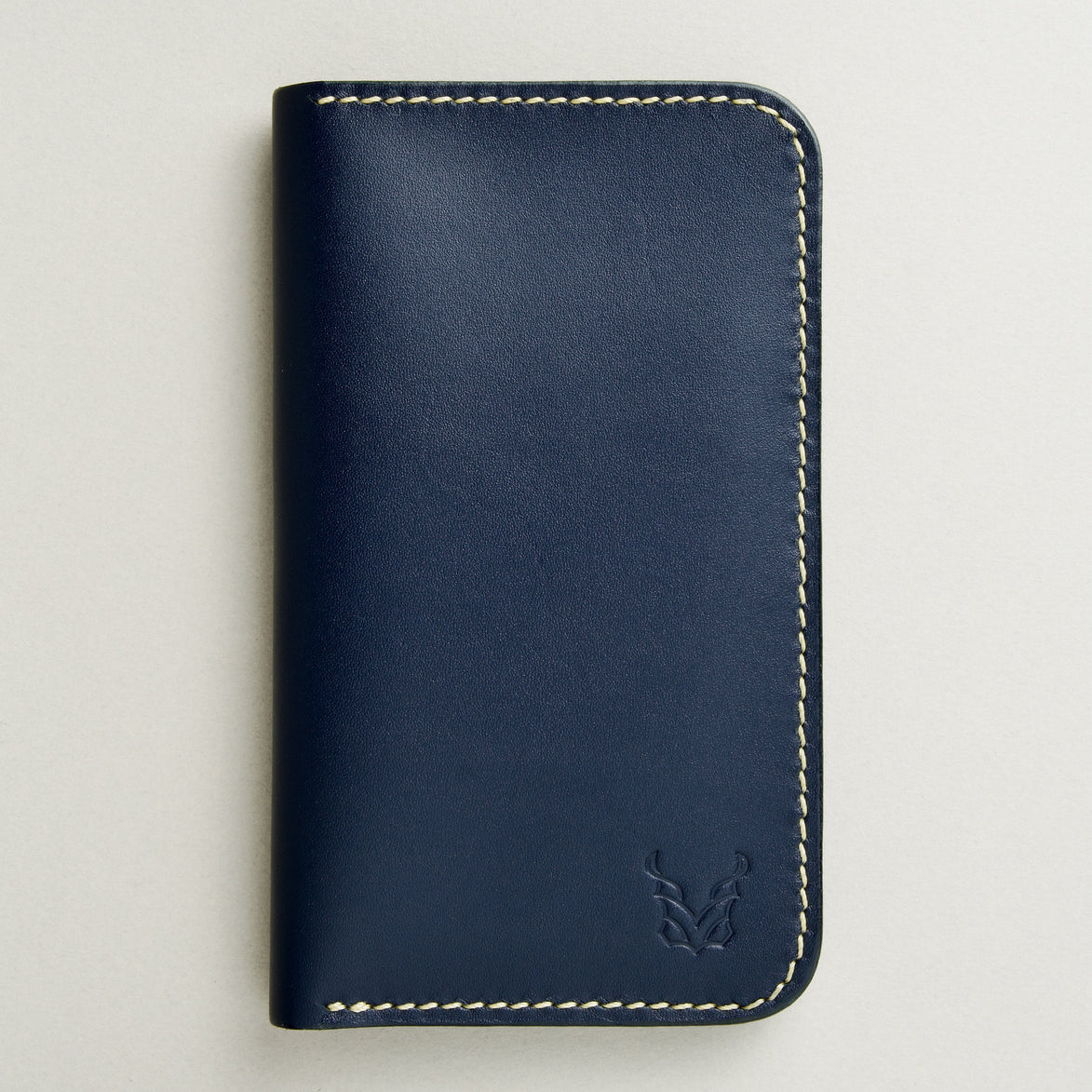 front view of vertical full-grain leather bifold wallet in dark blue, featuring handmade stitching in ivory and embossed logo. Markore Karakoram II.