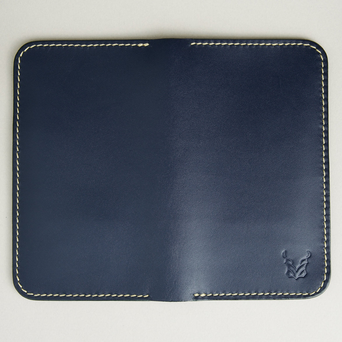 Unfolded back view of vertical full-grain leather bifold wallet in Dark Blue, featuring handmade stitching in ivory and embossed logo. Markore Karakoram II.
