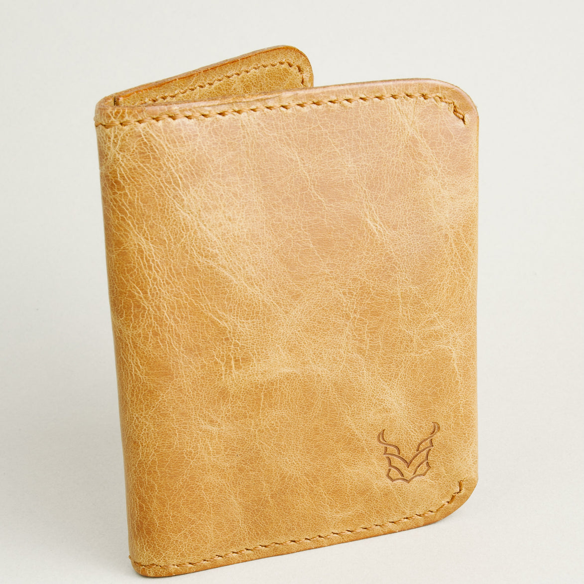 Side view of leather bifold wallet in natural, featuring handmade stitching and embossed logo. Markore Natural.