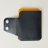 Back view of full grain leather card holder in black and amber, featuring an open side flap with two stainless steel press buttons and red handmade stitching. Markore Niva Glide.