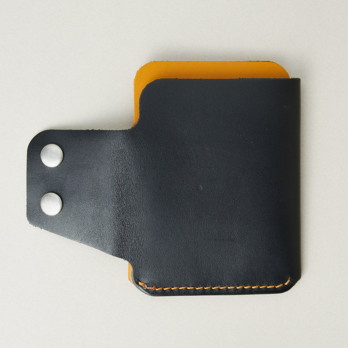 Back view of full grain leather card holder in black and amber, featuring an open side flap with two stainless steel press buttons and red handmade stitching. Markore Niva Glide.