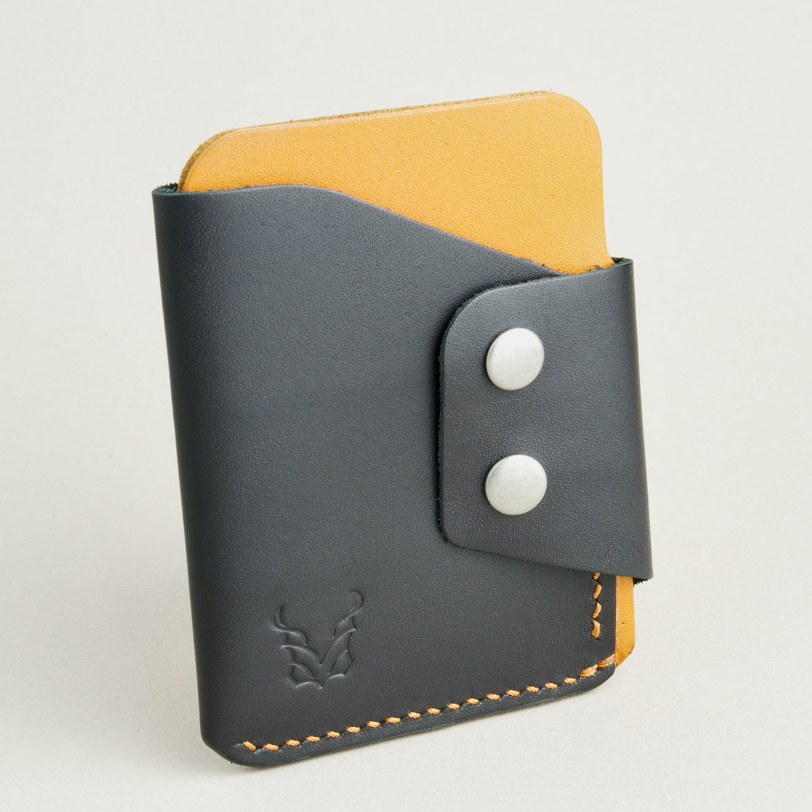 Side view of full grain leather card holder in black and amber, featuring side flap with two stainless steel press buttons, amber handmade stitching and embossed logo. Markore Niva Glide.