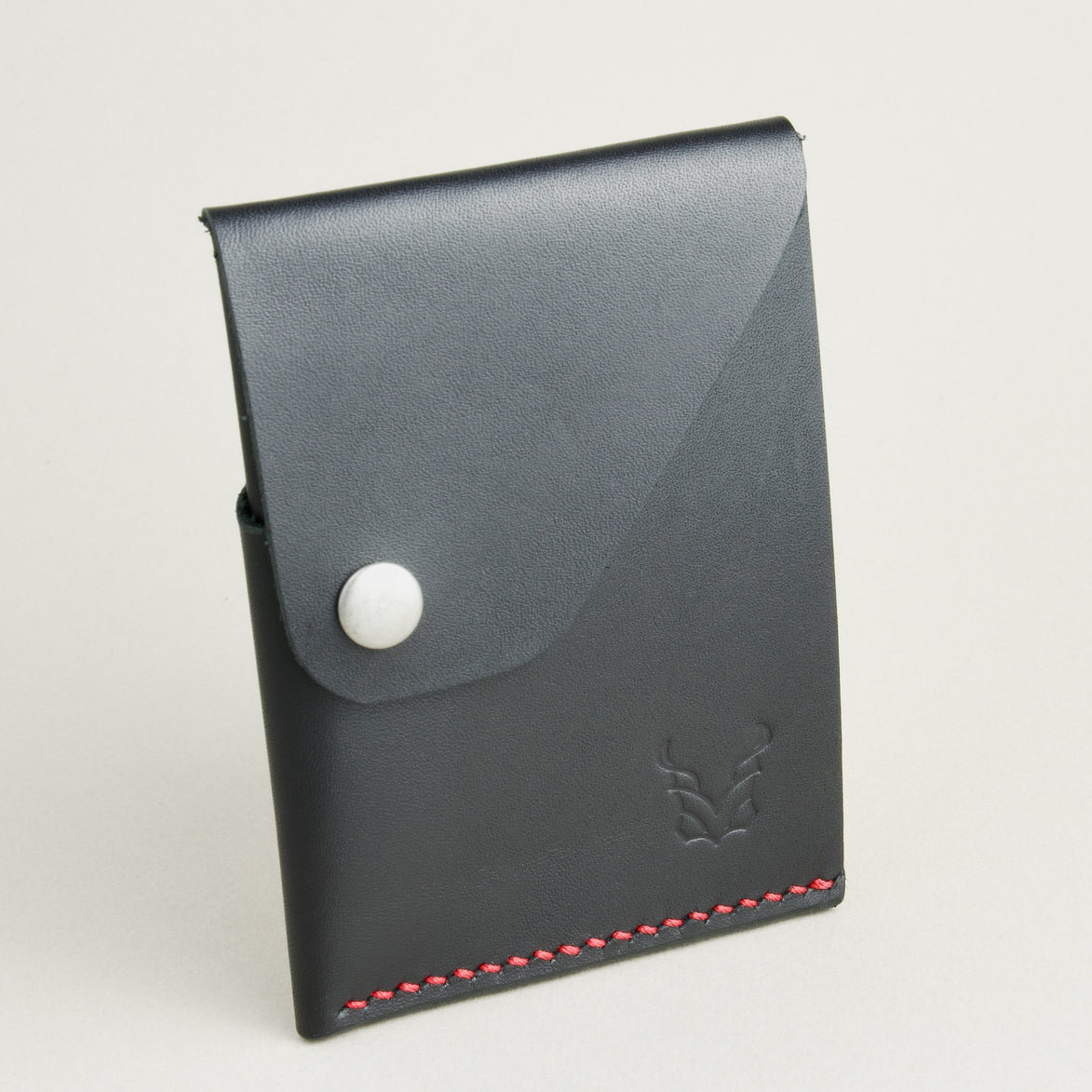 Side view of full grain leather card in midnight black with red handmade stitching, featuring a flap with stainless steel press button and embossed logo. Markore Niva Heritage.