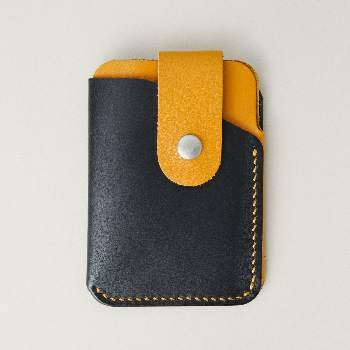 Front view of full grain leather card holder in midnight black and amber, featuring a leather loop with stainless steel press button and handmade stitching. Markore Niva Loop.