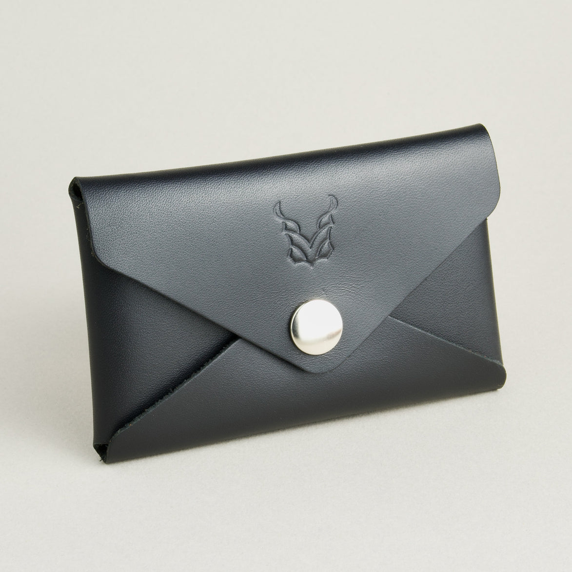 Side view of full grain leather envelope style wallet in midnight black with stainless steal press button and embossed logo. Markore Niva Seal.