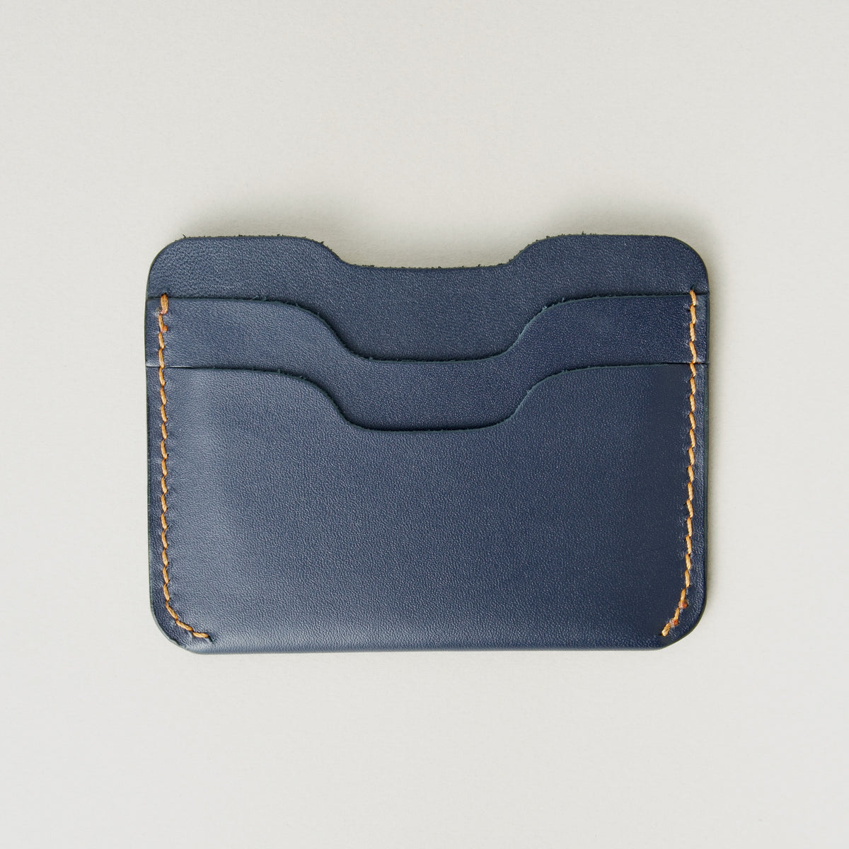 Back view of dark blue full-grain leather card sleeve featuring card slots and amber handmade stitching. Markore Niva Zoj.