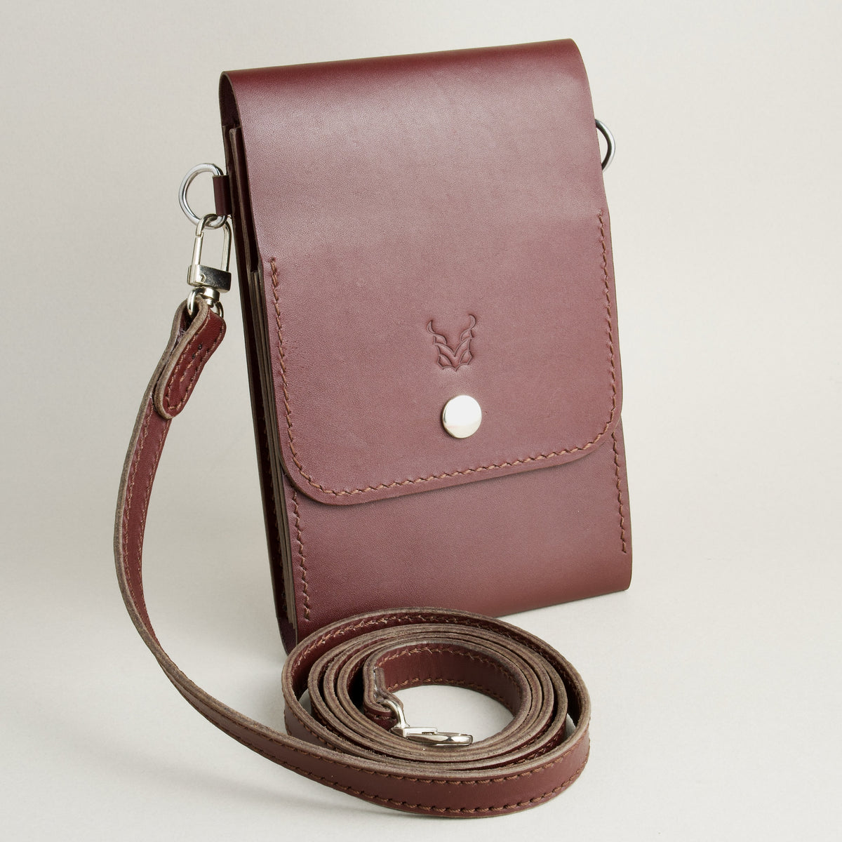Side view of vertical full-grain leather crossbody bag and matching shoulder strap in Espresso Brown, showing handmade stitching, embossed logo and stainless steel press stud. Markore Nora Veldt.