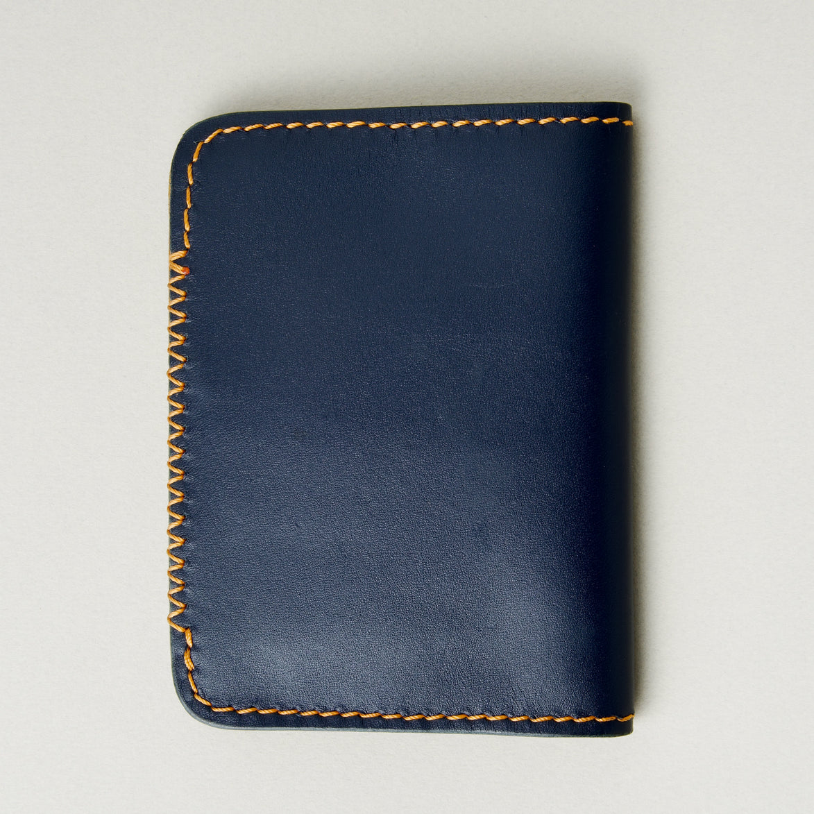 Back view of dark blue full-grain leather wallet highlighting amber handmade cross stitch detailing along the edge. Markore Ravi Edge.