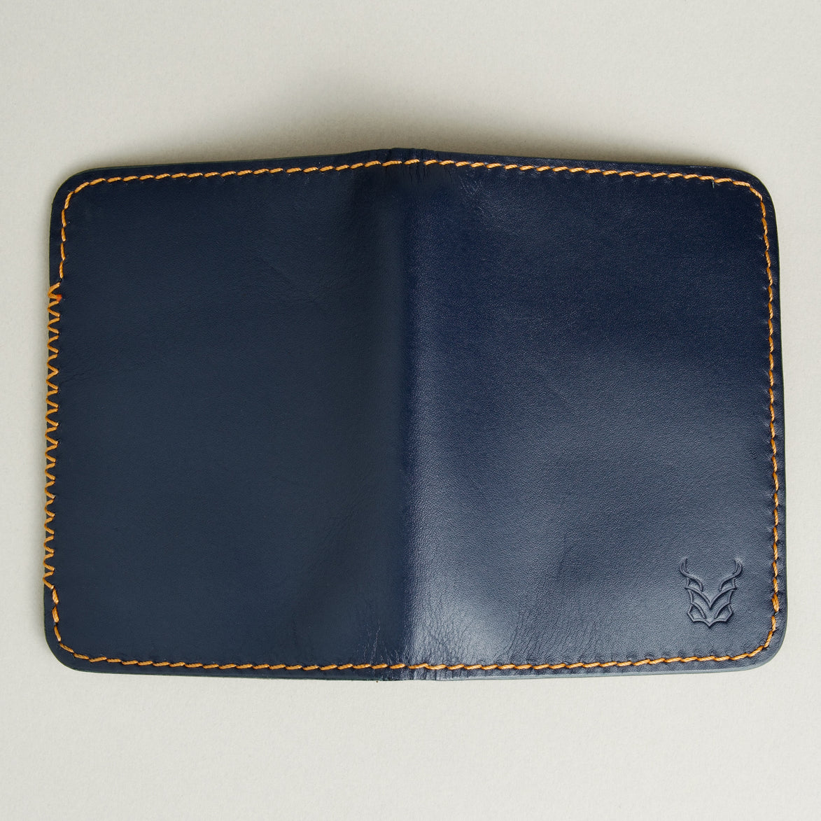 Outside view of dark blue full-grain leather wallet featuring amber handmade stitching, cross stitch detailing and embossed logo. Markore Ravi Edge
