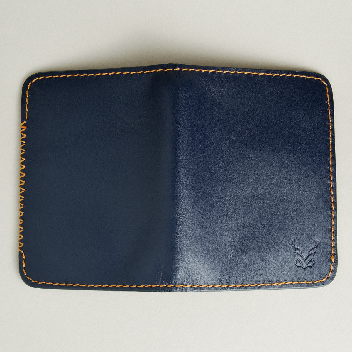 Outside view of dark blue full-grain leather wallet featuring amber handmade stitching, cross stitch detailing and embossed logo. Markore Ravi Edge