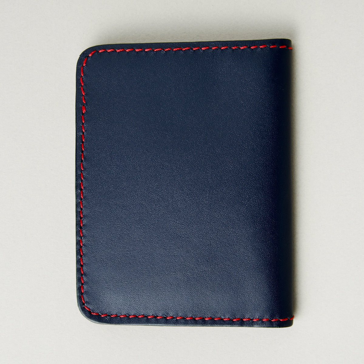 Back view of dark blue full-grain leather wallet featuring red handmade stitching. Markore Ravi Fold.
