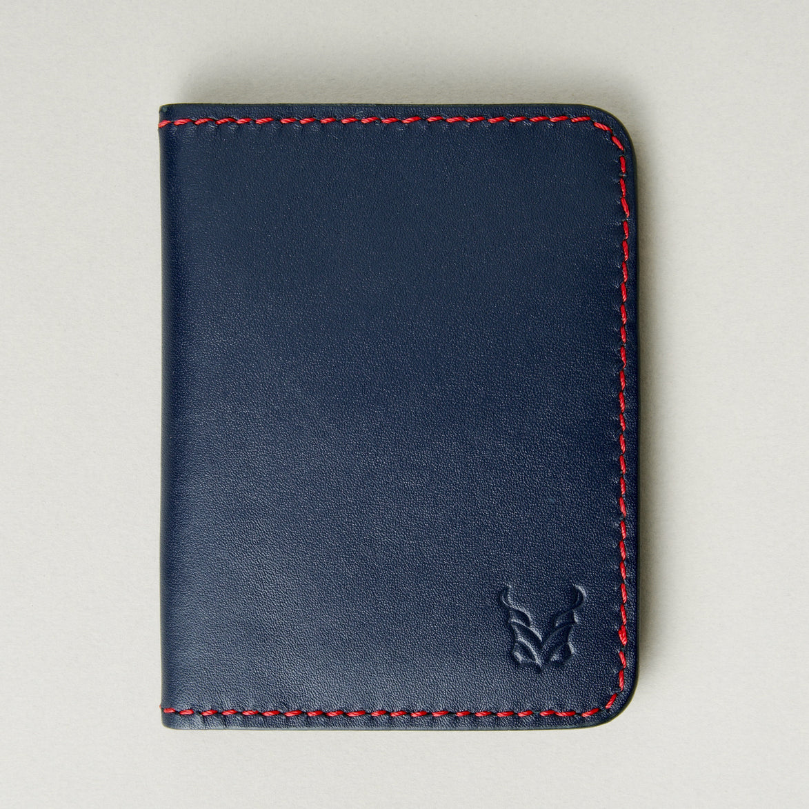 Front view of dark blue full-grain leather wallet featuring red handmade stitching and embossed logo. Markore Ravi Fold.