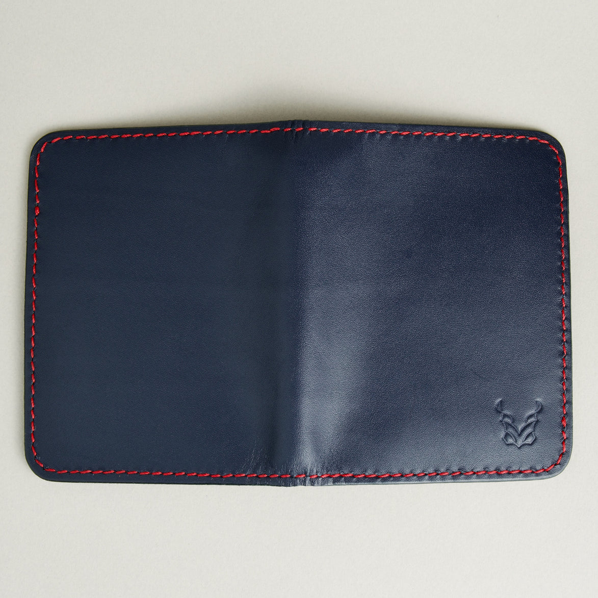 Outside view of dark blue full-grain leather vertical wallet featuring red handmade stitching and embossed logo. Markore Ravi Fold.
