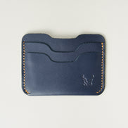 Front view of dark blue full-grain leather card sleeve featuring card slots, amber handmade stitching and embossed logo. Markore Niva Zoj.