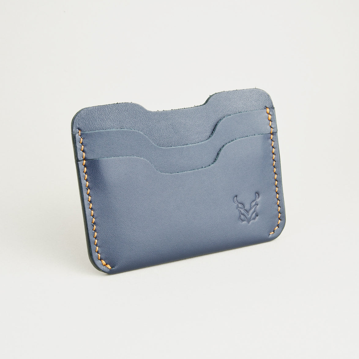 Side view of dark blue full-grain leather card sleeve featuring card slots, amber handmade stitching and embossed logo. Markore Niva Zoj.