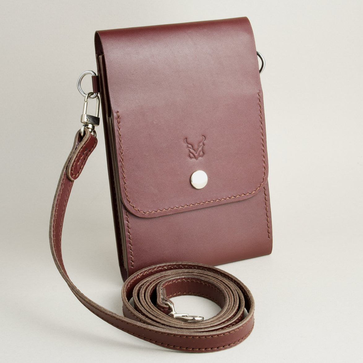 Side view of vertical full-grain leather crossbody bag and matching shoulder strap in Espresso Brown, showing handmade stitching, embossed logo and stainless steel press stud. Markore Nora Veldt.