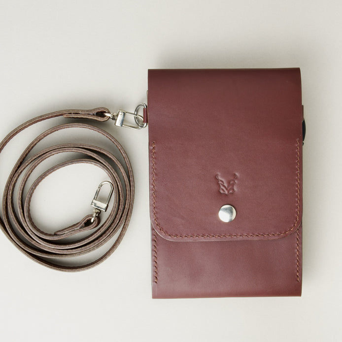 Front view of vertical full-grain leather crossbody bag and matching shoulder strap in Espresso Brown, showing handmade stitching, embossed logo and stainless steel press stud. Markore Nora Veldt.