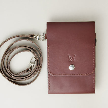 Front view of vertical full-grain leather crossbody bag and matching shoulder strap in Espresso Brown, showing handmade stitching, embossed logo and stainless steel press stud. Markore Nora Veldt.