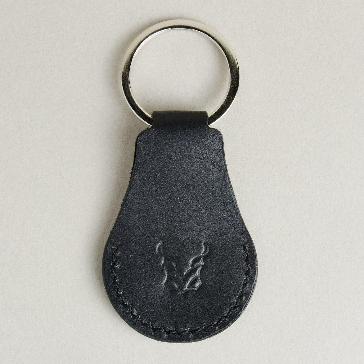 Back view of midnight black AirTag keychain in full-grain leather with round metal key ring and embossed logo. Markore Tag Mate.