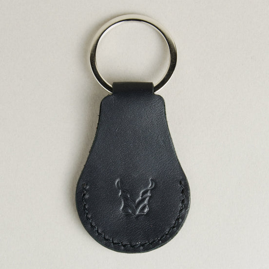Back view of midnight black AirTag keychain in full-grain leather with round metal key ring and embossed logo. Markore Tag Mate.