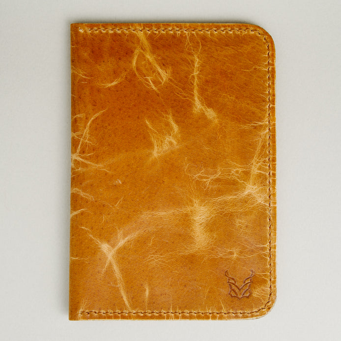 Front view of vertical full-grain leather passport holder in amber, featuring handmade stitching and embossed logo. Markore Voyage Pass.