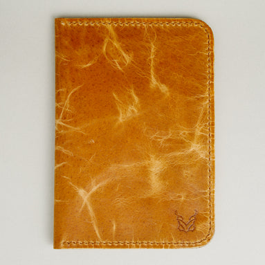 Front view of vertical full-grain leather passport holder in amber, featuring handmade stitching and embossed logo. Markore Voyage Pass.