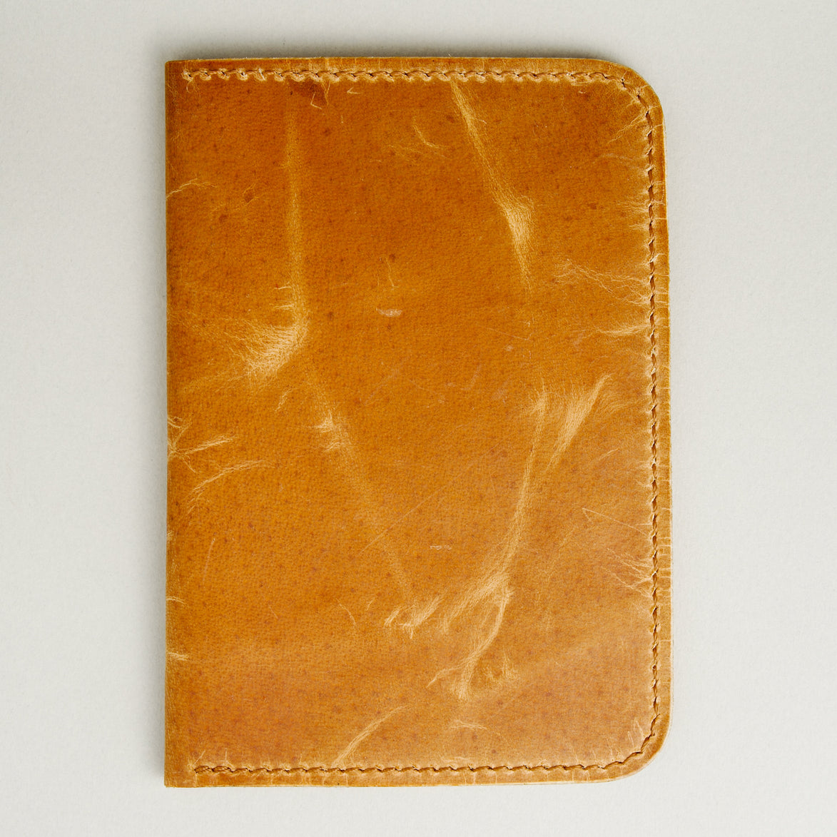 Backside view of vertical full-grain leather passport holder in amber, featuring handmade stitching. Markore Voyage Pass.